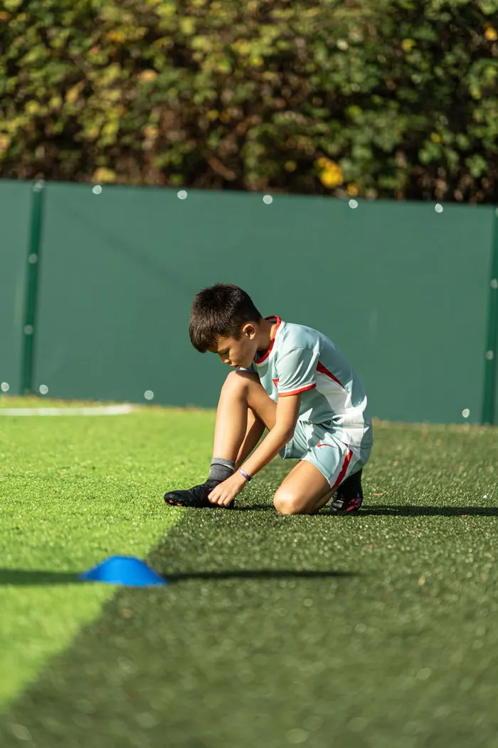 A young player kneeling to tie his boot